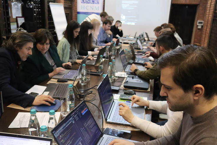 People working on laptops around a large table in a collaborative setting.