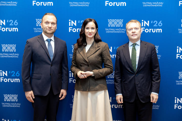 Three people in formal attire standing against a blue backdrop with text, appearing at a professional event.