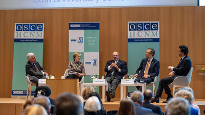Panel of five people discussing on stage at a conference, seated with microphones, facing an audience.