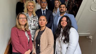 Group of people smiling, standing on a staircase with ornate railings in a well-lit interior.