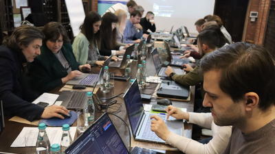 People working on laptops around a large table in a collaborative setting.