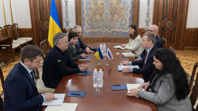 Meeting in a formal room, two groups of people sit across a table with Ukrainian and EU flags in the background.