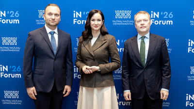 Three people in formal attire standing against a blue backdrop with text, appearing at a professional event.