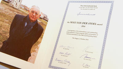 A person in a coat beside an award certificate with blue border and signatures.